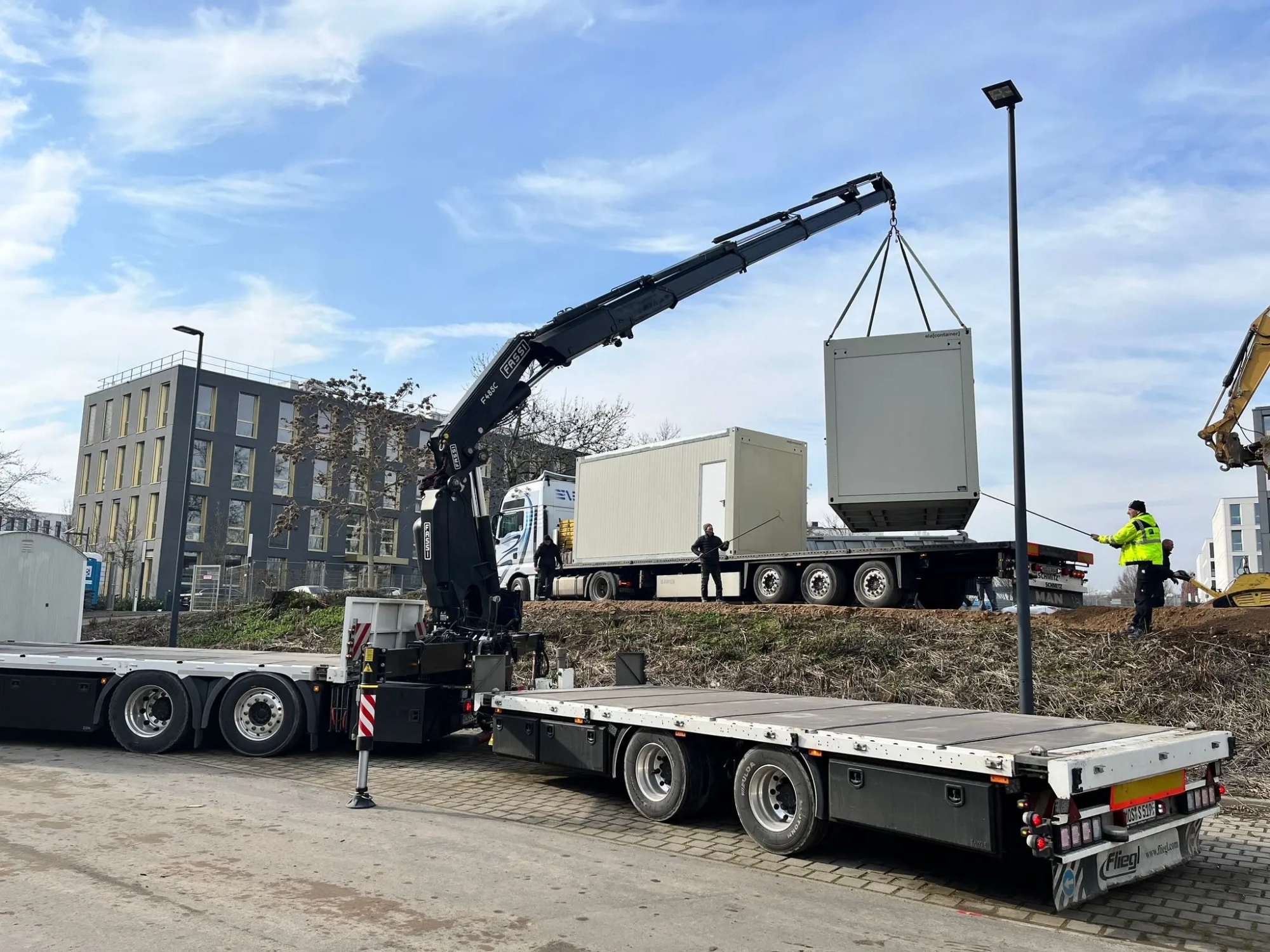 4d42af57-90f7-4248-bfd8-3c2988e7e1c1 Kran hebt einen Container beim Containertransport an einer städtischen Baustelle